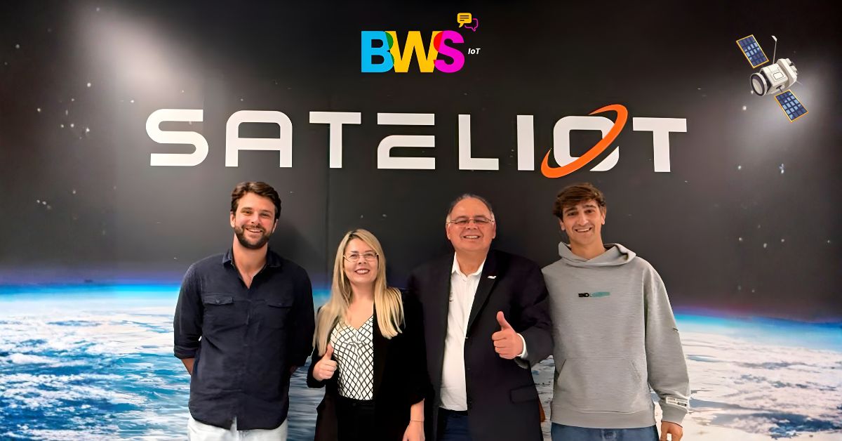 Equipe da BWS IoT em visita à Sateliot, posando em frente ao logo da sateliot em painel com imagem da Terra vista do espaço.